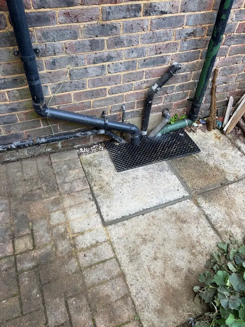 Reinstated surface beside a drainage grille after water supply pipe installation.