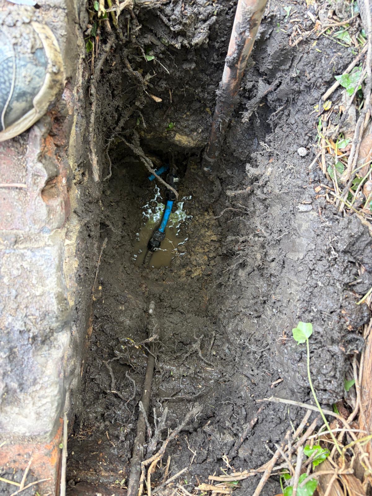Active water main leak found during excavation in Sussex — blue MDPE pipe with water pooling