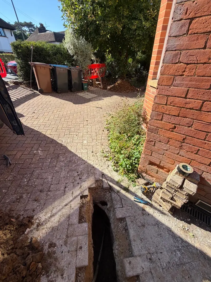 Water supply pipe installation working area with an excavation through block paving in Oxted.