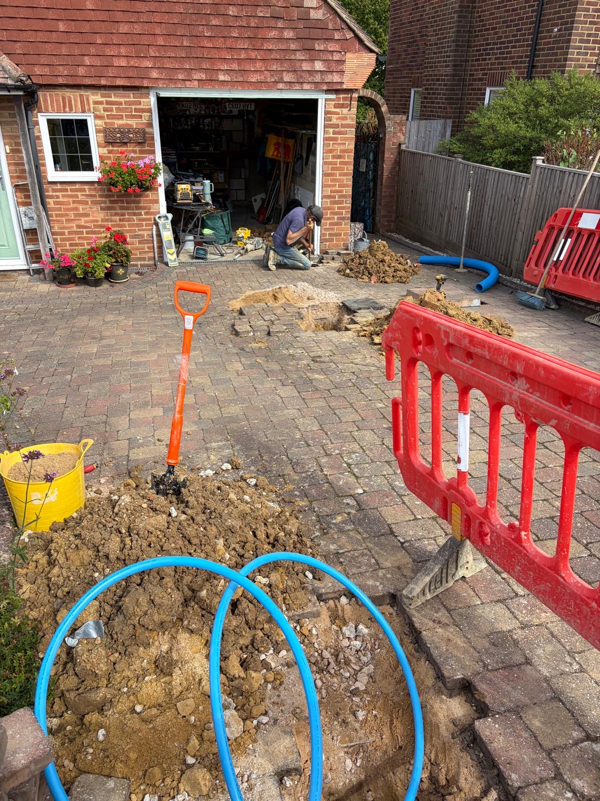 Water main replacement in East Grinstead — access excavations across a block paved driveway with new blue MDPE supply pipe.