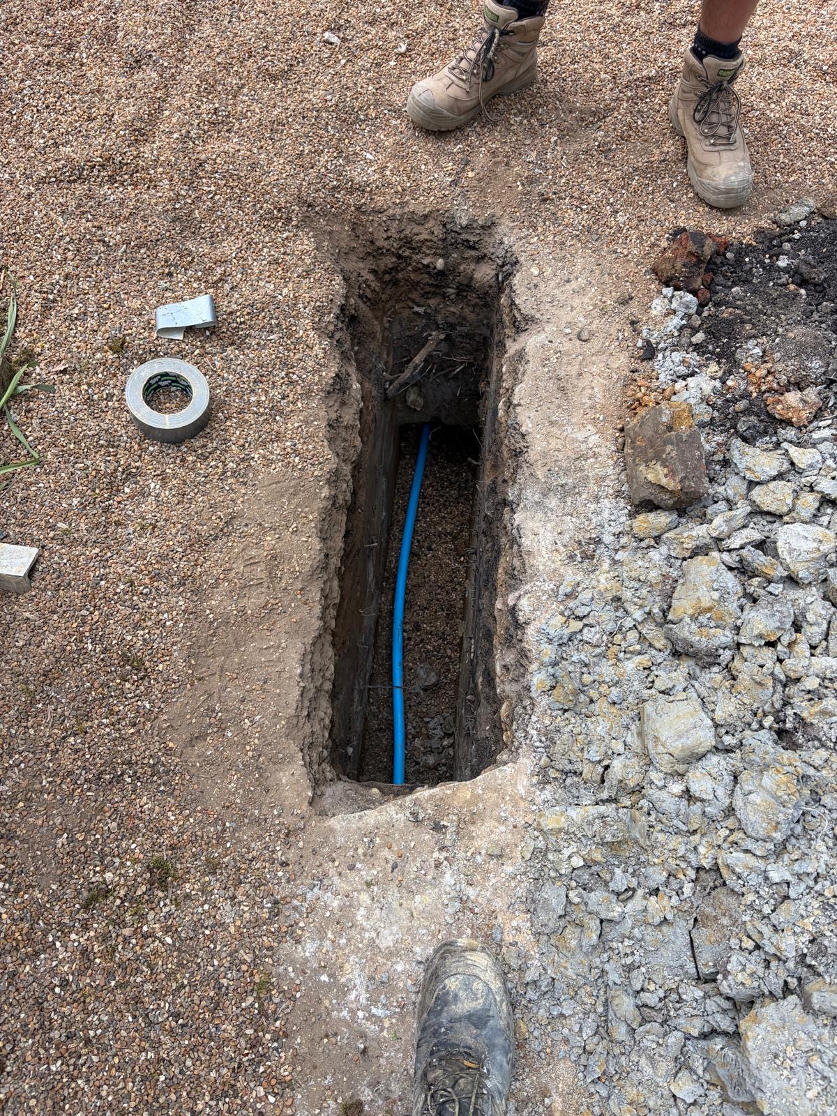Moling access pit showing new blue MDPE pipe being installed through concrete surface — East Grinstead